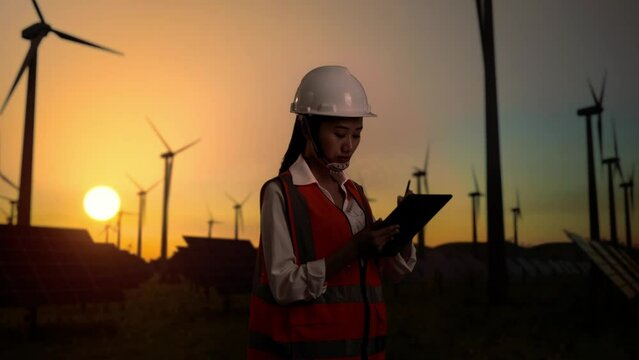 Asian female engineer takes note on a tablet in the wind turbines rotating 
