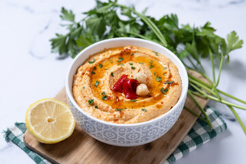 Roasted red pepper hummus in white bowl on white marble background.