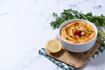 Roasted red pepper hummus in white bowl on white marble background. Copy space