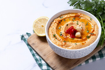 Roasted red pepper hummus in white bowl on white marble background. Copy space