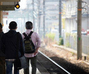 朝の通勤時間帯の駅のホームで歩く男性たちの姿