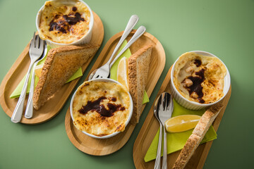 Typisches DDR Würzfleisch Ragout Fin mit Käse überbacken, Zitrone, Toast Brot und Worcester Sauce  in Auflaufform Schale auf Holz Bambus Tablett mit Serivette und Besteck auf grün Hintergrund
