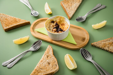 Typisches DDR Würzfleisch Ragout Fin mit Käse überbacken, Zitrone, Toast Brot und Worcester Sauce  in Auflaufform Schale auf Holz Bambus Tablett mit Serivette und Besteck auf grün Hintergrund