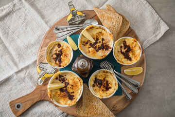 Typisches DDR Würzfleisch Ragout Fin mit Käse überbacken, Zitrone, Toast Brot und Worcester Sauce  in Auflaufform Schale auf Holz Brett, Tuch und hell grau Stein Hintergrund
