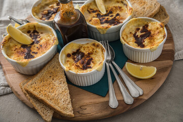 Typisches DDR Würzfleisch Ragout Fin mit Käse überbacken, Zitrone, Toast Brot und Worcester Sauce  in Auflaufform Schale auf Holz Brett, Tuch und hell grau Stein Hintergrund