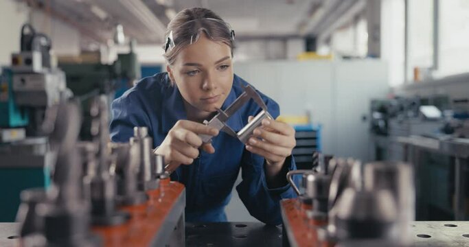 Apprentice measuring metal bolt with caliper in workshop