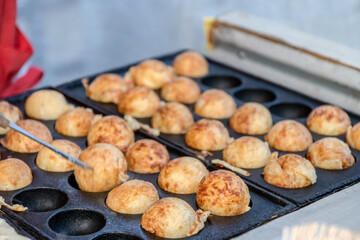 Cooking Takoyaki made of a wheat flour-based and cooked in a special moulded in a shape of little round balls containing pieces of octopus. Famous street food in Japan.