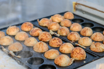 Cooking Takoyaki made of a wheat flour-based and cooked in a special moulded in a shape of little round balls containing pieces of octopus. Famous street food in Japan.