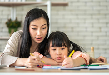 Obraz premium Portrait happy love asian family mother teach little daughter asian girl learn and study on table.Mom and asian young girl writing with book and pencil making lessons in homeschool at home.Education