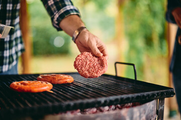 A man putting a slice of raw meat on the grill, making a barbecue outdoors.