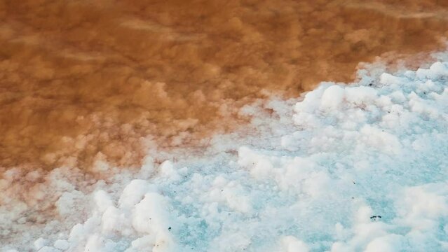 Mineralogy. Shore of hypersalted lake (self-settling salt lake) with deposition of salt crystals (solar salt). Red-brown water is determined by bacterias Dunaliella salina and Salinibacter ruber