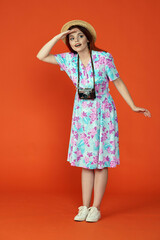 Woman in hat standing holding hand over forehead looking for something with curious face,isolated on orange background. Portrait of female traveler.