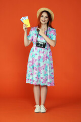 Woman standing holding flight tickets and passport, pointing at it and smiling at the camera, isolated on orange background. Portrait of female traveler.
