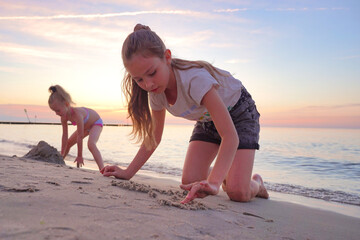 Two little girls are playing in the sand on the beach.