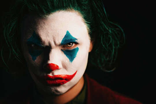 Woman with make-Up joker. Green-haired lady. Costume for Halloween. Sad clown face on black background.