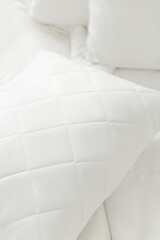 White quilted pillow on a white bedding white background. Cushion. Home textile. Close up photo, top view