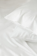 Two white pillows in satin or silk or lyocell pillowcases on white sheet. Bedding and accessories. Home textile - obrazy, fototapety, plakaty