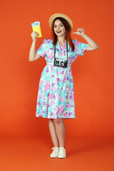 Woman looking at the camera smiling, holding flight tickets showing thumbs up at herself, isolated on orange background. Portrait of female traveler.