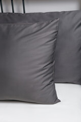 Two dark grey pillows in satin or silk or lyocell pillowcases on white sheet. Bedding and accessories. Home textile