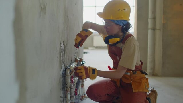 Female plumber screwing pipes to wall at construction site