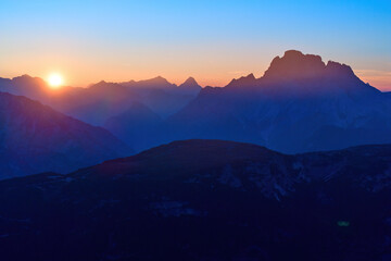 View of the Dolomites panorama with the setting sun in the dark blue evening sky. Shades of orange, dark blue to purple. A moment of calm, a sense of space. Autumn on a hike in the Dolomites, Italy.