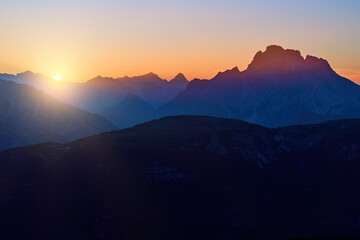 View of the Dolomites panorama with the setting sun in the dark blue evening sky. Shades of orange, dark blue to purple. A moment of calm, a sense of space. Autumn on a hike in the Dolomites, Italy.