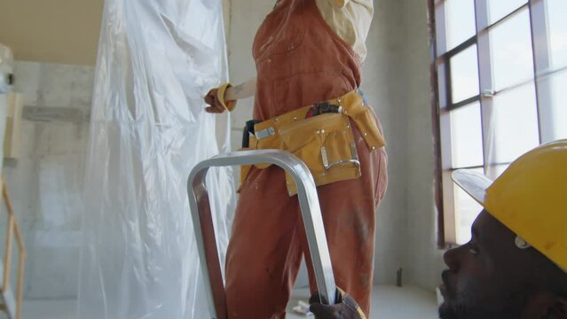 Tilt up shot of builders covering part of room with oilcloth