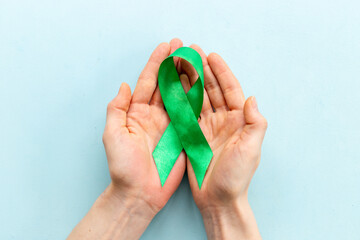 Green ribbon symbol of why cancer and mental health with hands. Medical support concept