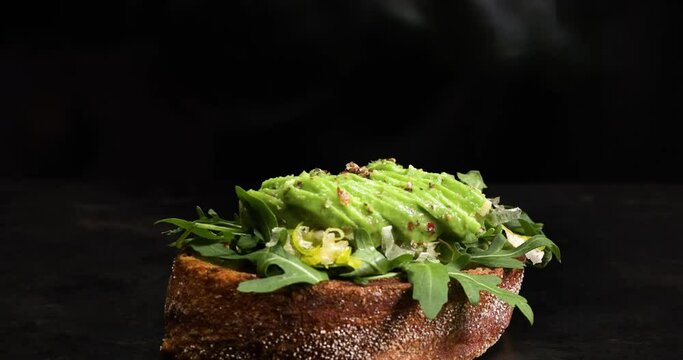 Sliced avocado is put onto a piece of bread topped with rocket