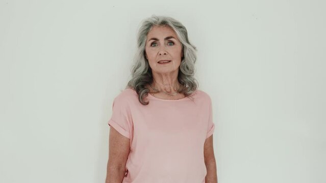 Serious senior lady poses in front of white wall