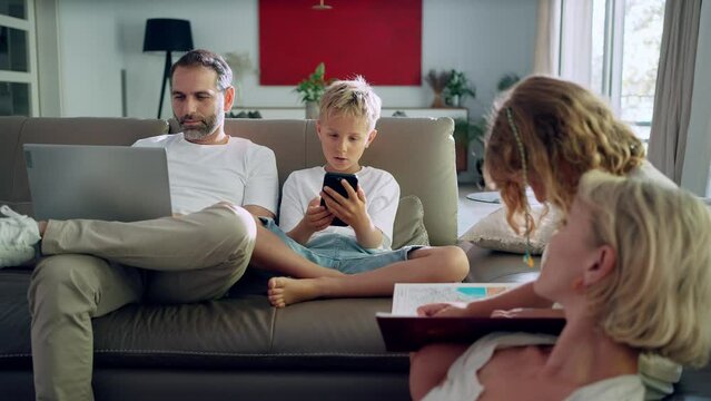 Family sitting on a sofa using laptop and smartphone and reading book
