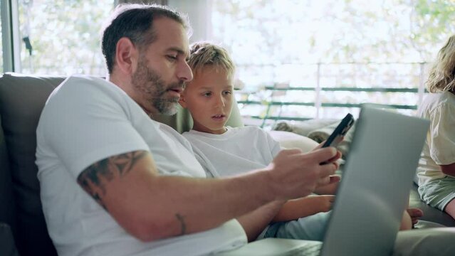 Father and son sitting on a sofa using laptop and smartphone