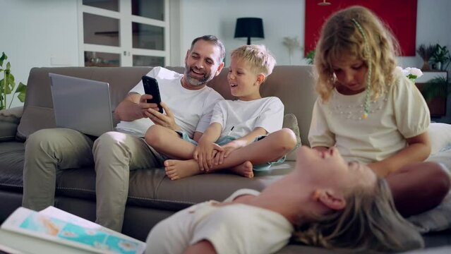 Family sitting on a sofa using laptop and smartphone and having fun