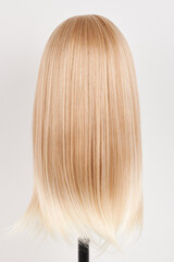 Fototapeta premium Natural looking blonde wig on white mannequin head. Long hair on the plastic wig holder isolated on white background, back view.