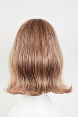 Natural looking dark brunet wig on white mannequin head. Middle length brown hair on the plastic wig holder isolated on white background, back view.