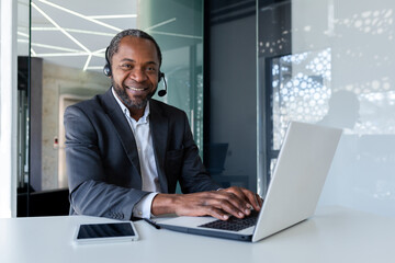 Portrait of african american businessman inside office at workplace, mature man using headset phone...