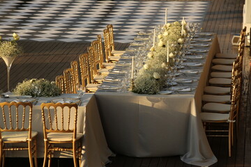 Decorated white wedding table for a festive dinner with pink flowers in brass pots on green lawn...