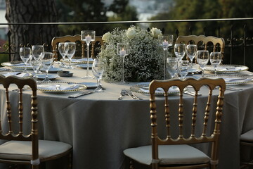 Decorated white wedding table for a festive dinner with pink flowers in brass pots on green lawn under the open sky.