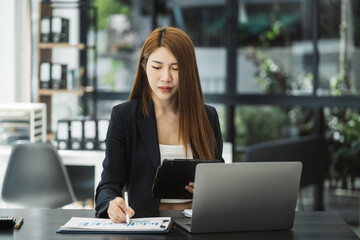 Businesswomen using tablet with laptop and document on desk in modern office.