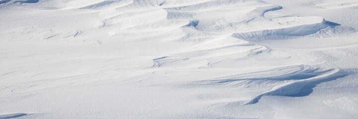 Fototapeta na wymiar Snow texture. Wind sculpted patterns on snow surface. Wind in the tundra and in the mountains on the surface of the snow sculpts patterns and ridges. Arctic, Polar region. Winter panoramic background.