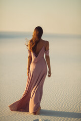 Walking romantic fashionable woman model in the desert in evening pink dress.Back view of gorgeous...