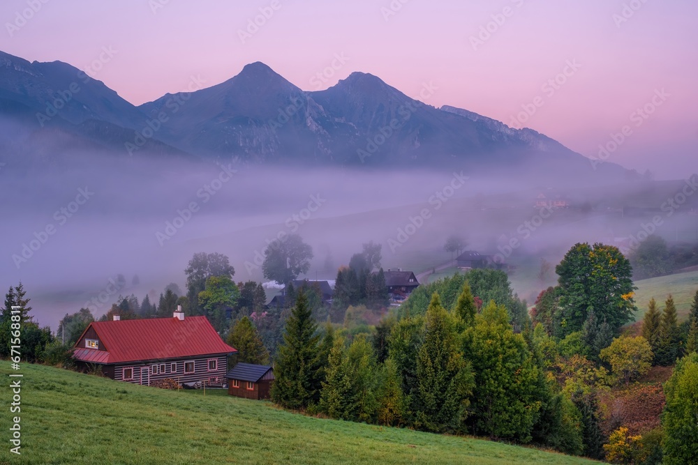 Wall mural Autumn foggy morning in an old village with wooden houses under mountain peaks