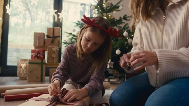 Caucasian girl and mother wrapping Christmas gifts on the floor. Shot with RED helium camera in 8K.   