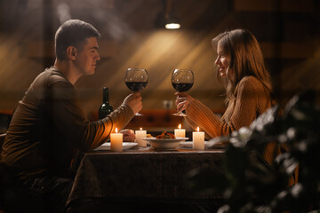 Trough window view on young couple in love drinking wine, celebrating Valentines day dining at...
