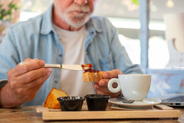 Blurred bearded senior man having breakfast in coffee shop while works on laptop. Elderly man...