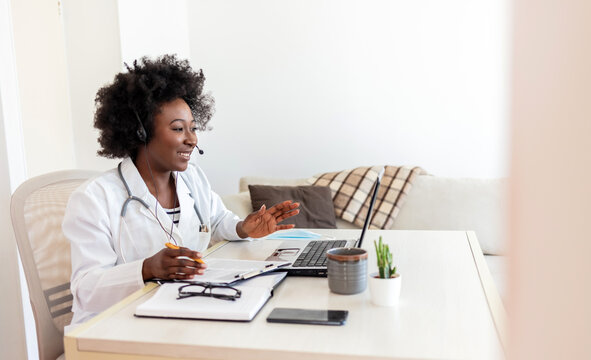 African American Woman Doctor Working At Her Office Doing Telemedicine Services. Helping Patients Online And By The Laptop. Primary Care Consultations.