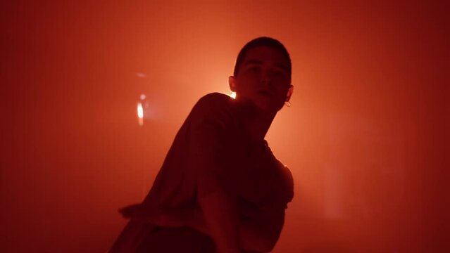 Young man dancing contemporary hip hop on red neon background in studio wearing white shirt. Shooting of modern slow dance choreography. Motion of male dancer expressing feelings in dance movings. 