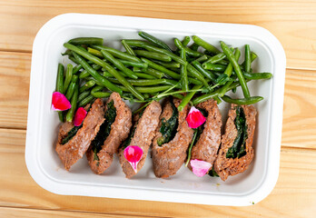 Veal roll with spinach and asparagus beans. Healthy diet. Takeaway food. Eco packaging. On a wooden background.