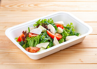 French salad with Camembert cheese. Healthy diet. Takeaway food. Ecological packaging. On a wooden background.