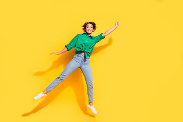 Fototapeta na wymiar Full length photo of pretty sweet lady wear green shirt jumping high catching arm empty space isolated yellow color background